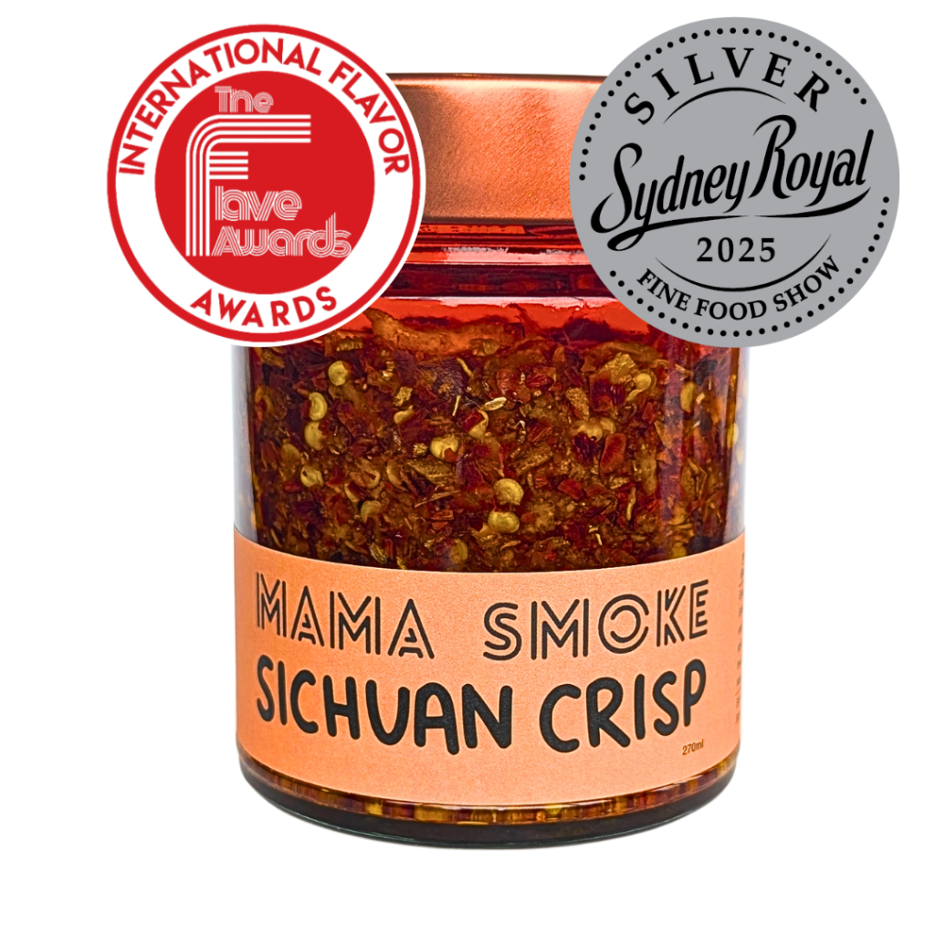 A jar of Mama Smoke Sichuan Crisp chili oil with topped with a copper-colored lid and an orange label. Two award seals are overlaid on the top: Winner International Flavor Awards 2026, and Silver Sydney Royal Fine Food Show 2025.